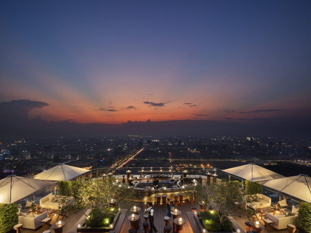 The Sora sky bar at Rosewood Phnom Penh overlooking the city skyline and Mekong River at sunset.